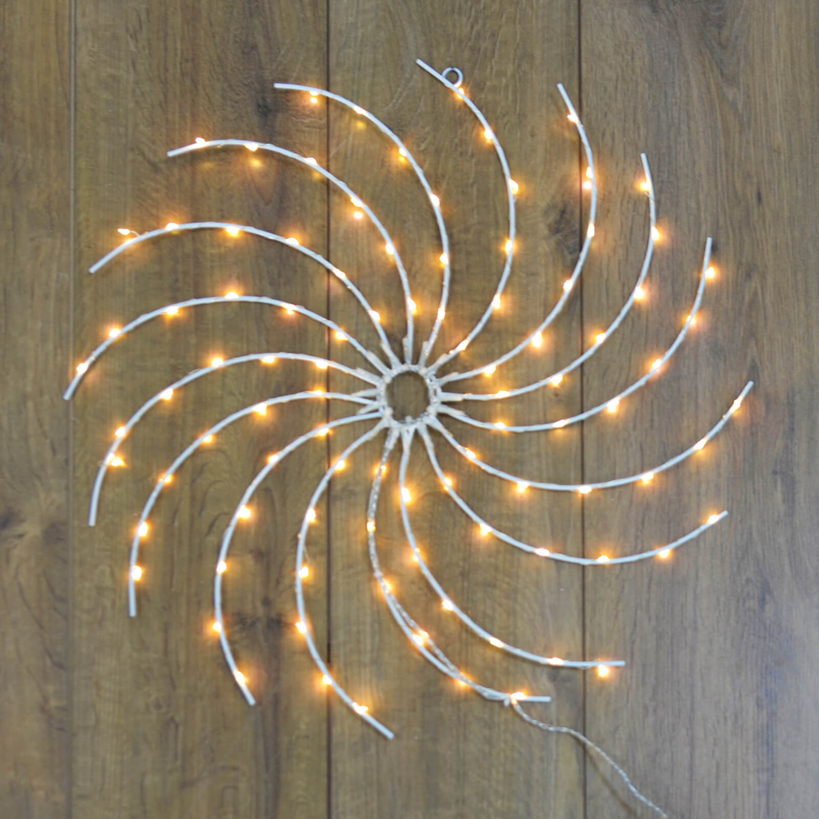 Light up swirl wheel Christmas wall decoration with warm white LED lights, hanging on a wood panelled wall